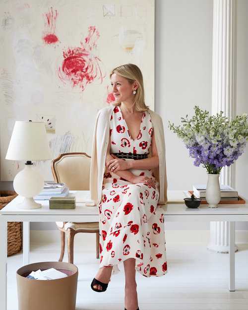 Top NYC Interior Designer sitting on white desk in red floral dress